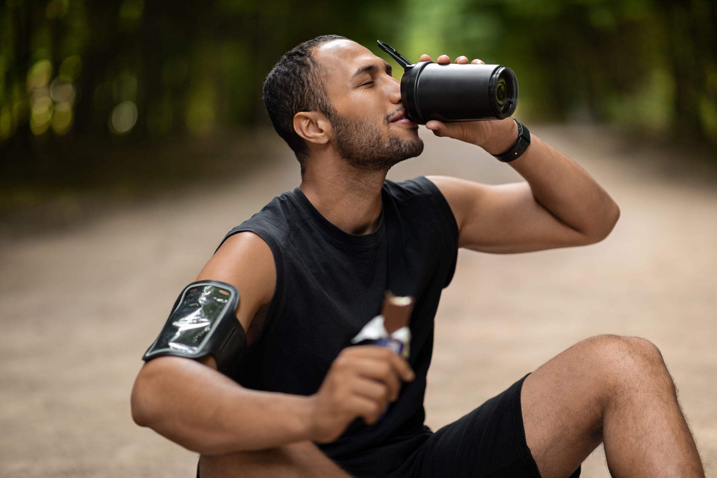 Hombre bebiendo batido rico en proteínas y comiendo barrita rica en proteínas después del entrenamiento