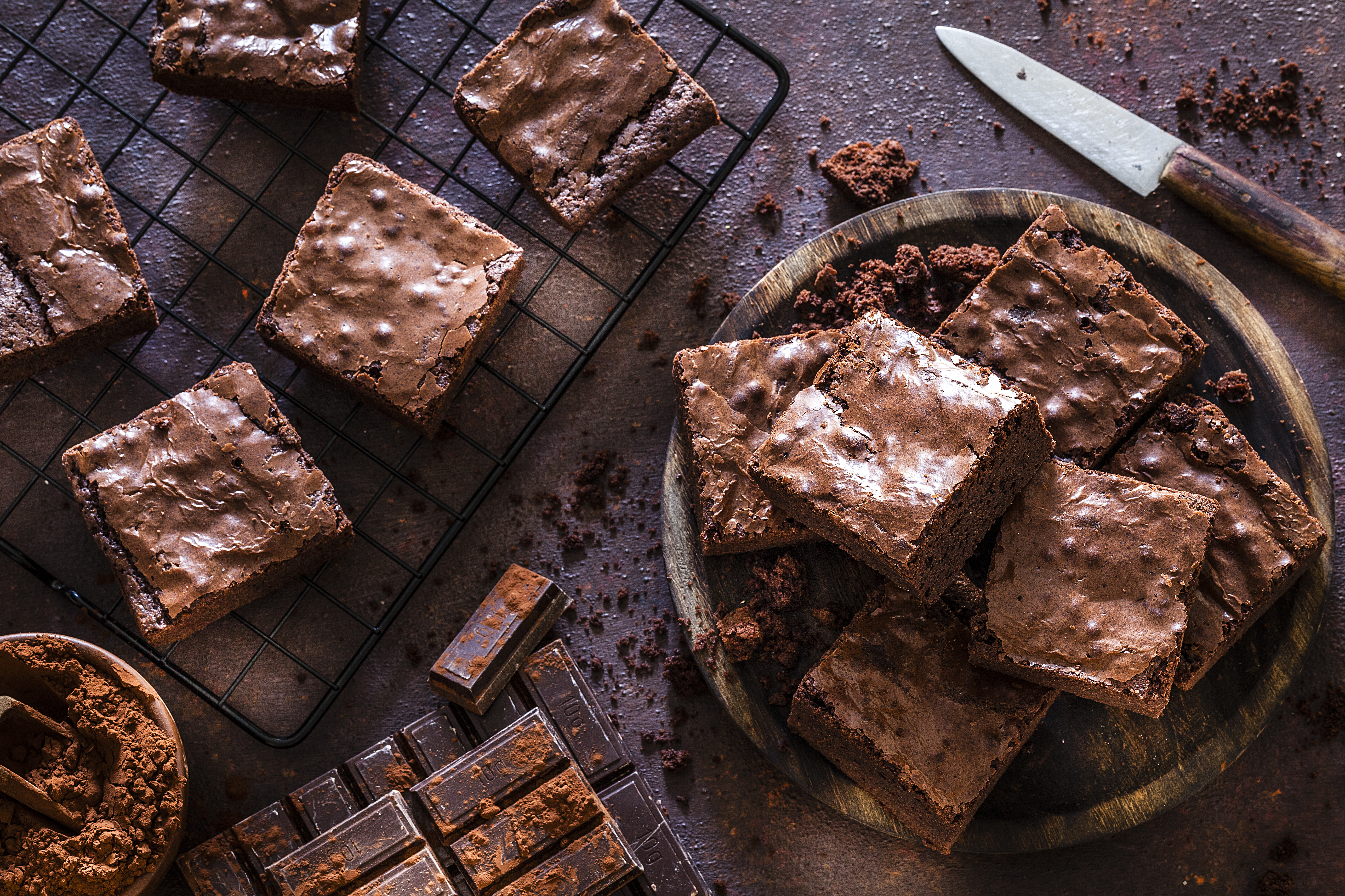 High Protein brownies stacked on a plate and on a cooling tray with a knife